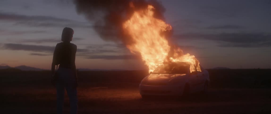 Woman watches a vehicle burn outside at night
