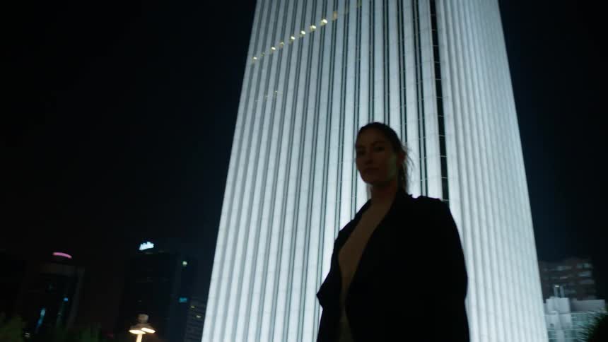 A woman walks past a tall lit building