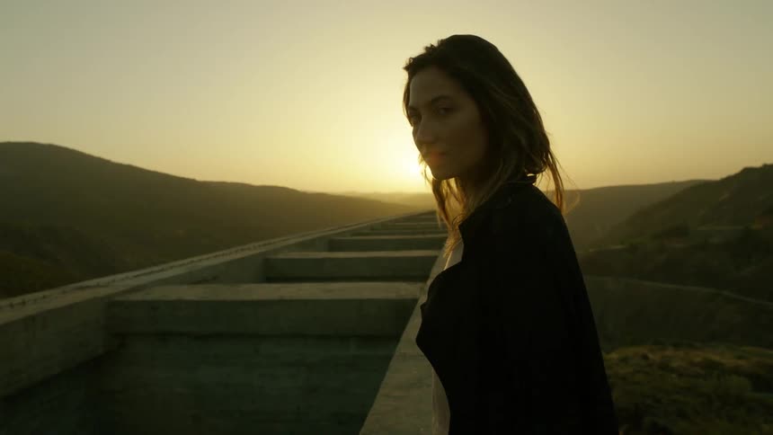 Woman standing next to a structure outdoors at sunset