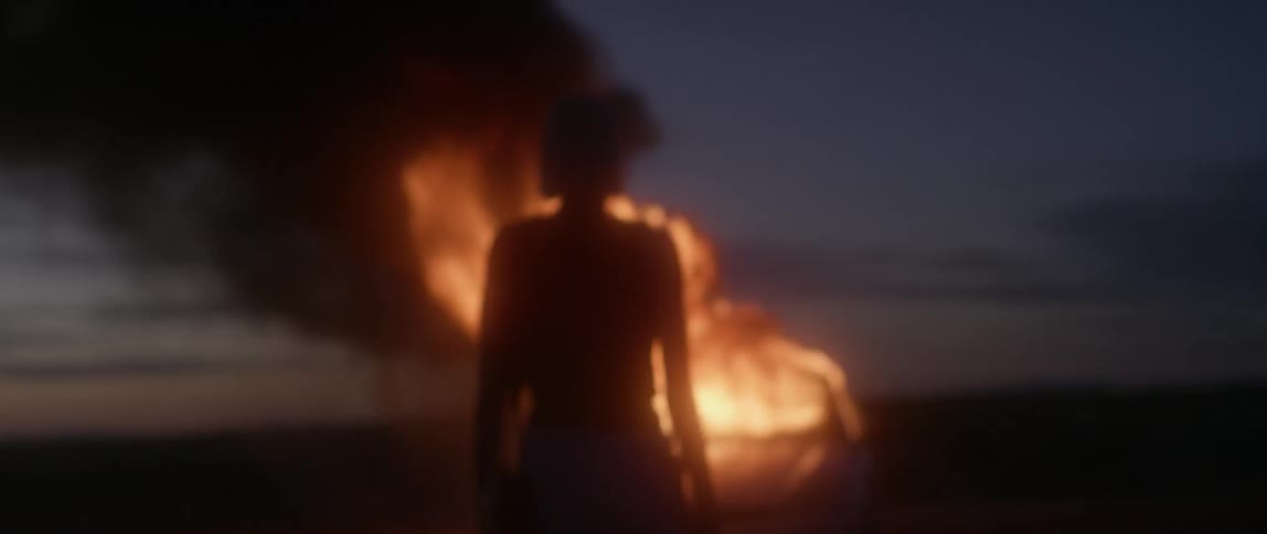 A woman walks towards a burning car