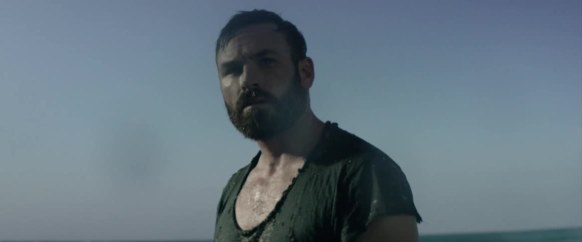 A man in tattered clothing looks up at something in the distance
