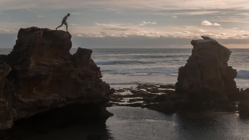 A man jumps off a rock ledge into the ocean