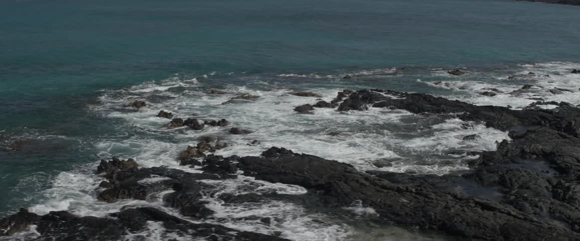 Ocean water crashing up onto rocky beach on sunny day