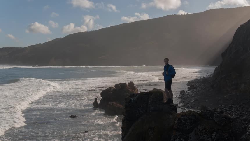 Man with a backpack stands on rocks near the water