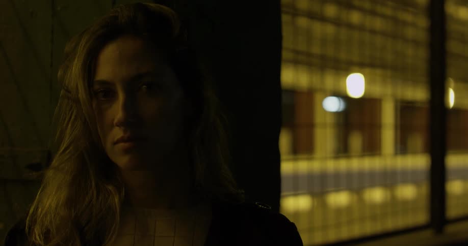 A woman leaning against a column looks up and stares