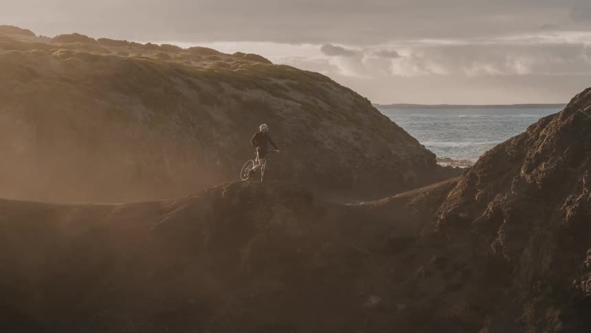 A person is riding their mountain bike on the hills by the water