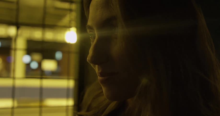 A woman smiles while standing next to a window at night