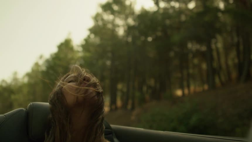 A woman leans back in the car seat as the wind blows her hair