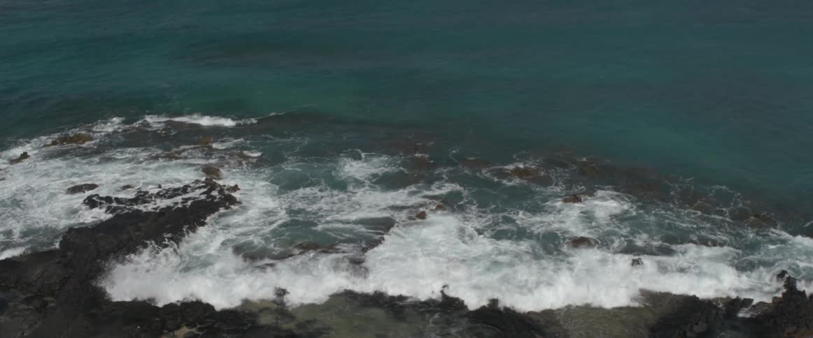 Ocean waves crashing onto rocky beach on sunny day