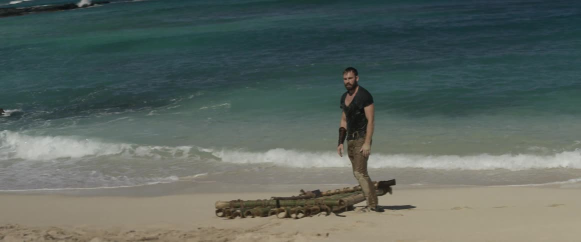 A man standing on the beach near a wood raft looks inland