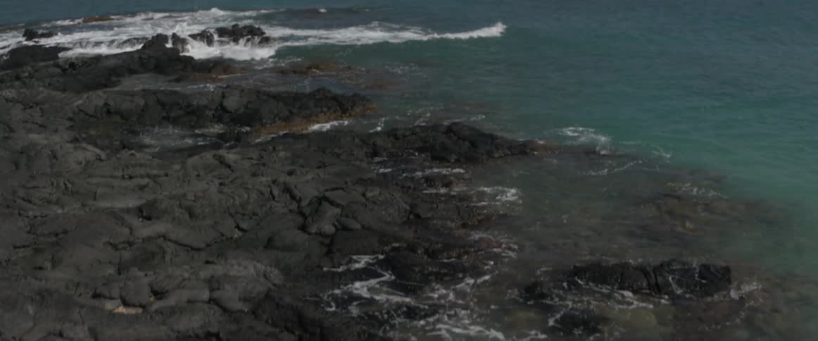 Waves roll ashore on a beach covered with lava rock