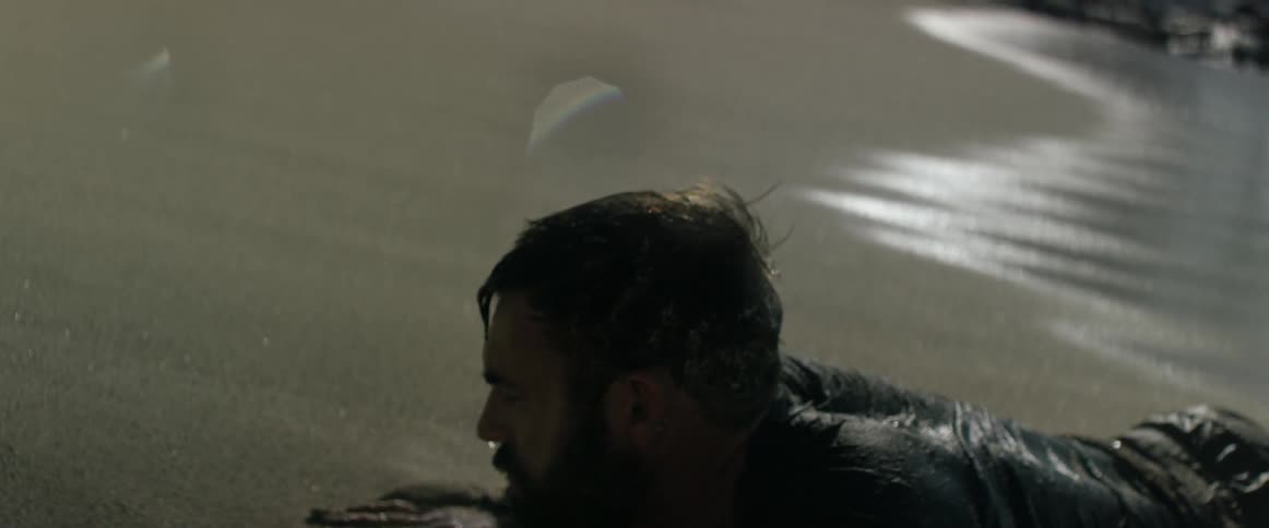 A man washed up on shore lifts his head then gets to his knees