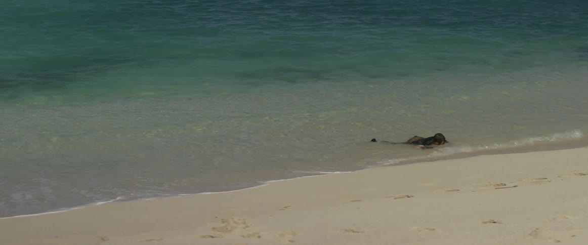 A man lying face down in the sand lifts his head as waves wash over him