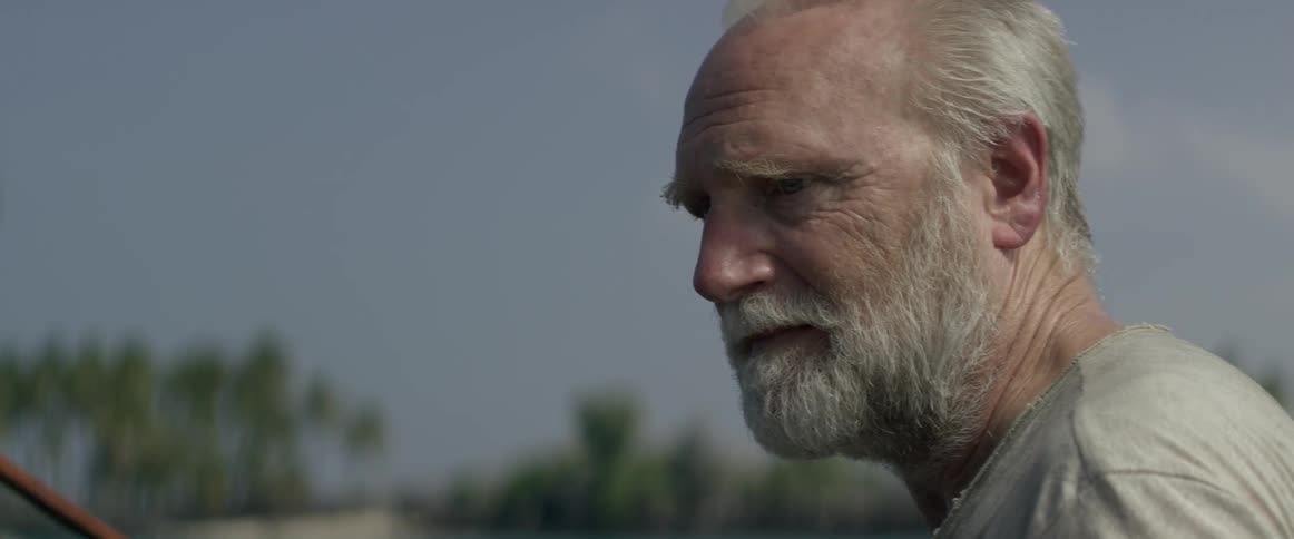 An elderly man listens to another man outside on a sunny day