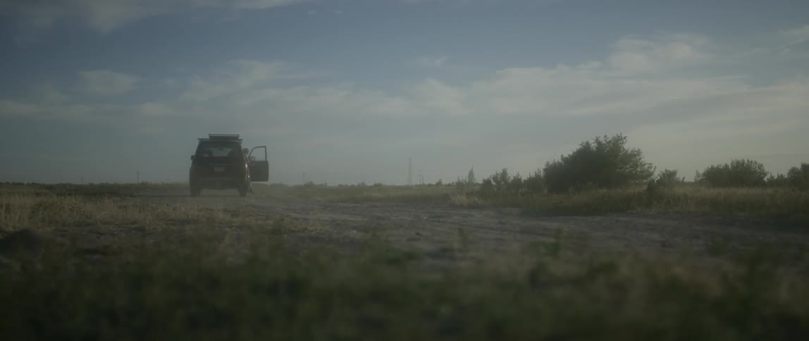 A car drives off into the field then stops to let a woman out