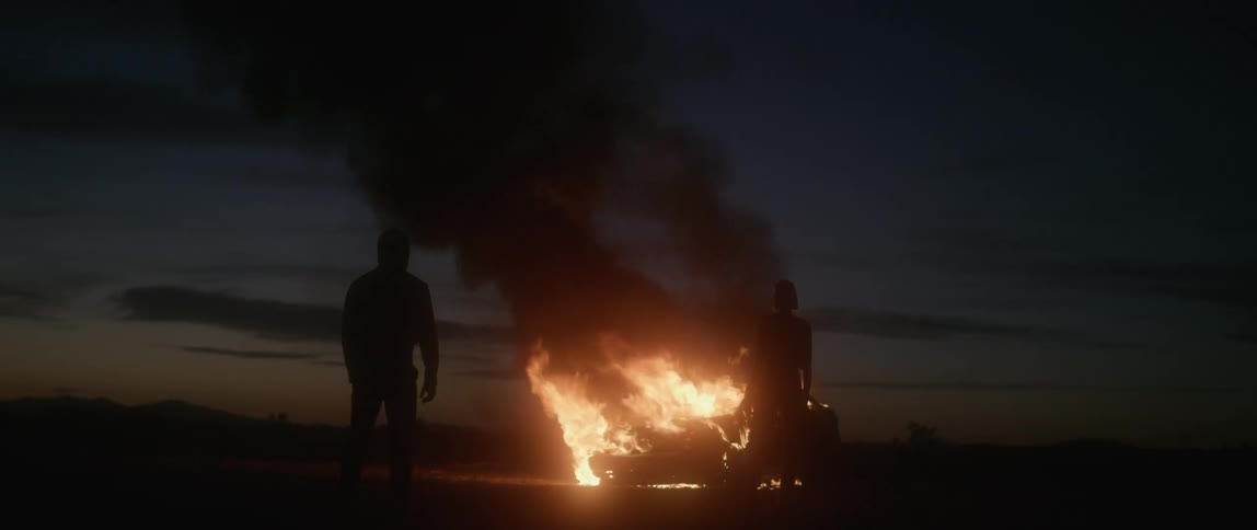 A man and woman watch a car burn