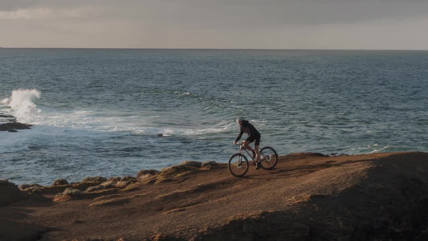 A person mountain bikes on a cliff by the beach