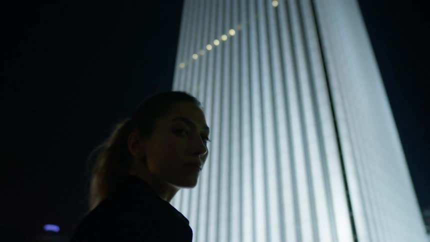 A woman stands in front of a lit skyscraper at night
