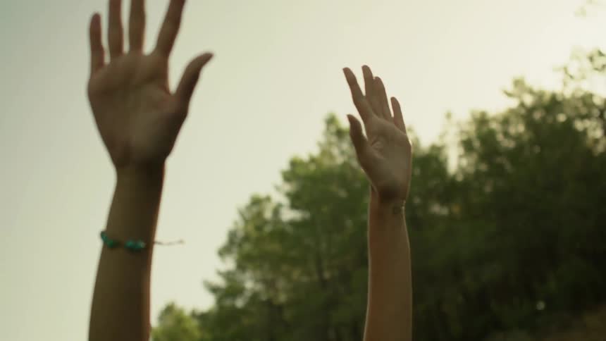 A woman rides with her hands in the air in a rural area at sunset