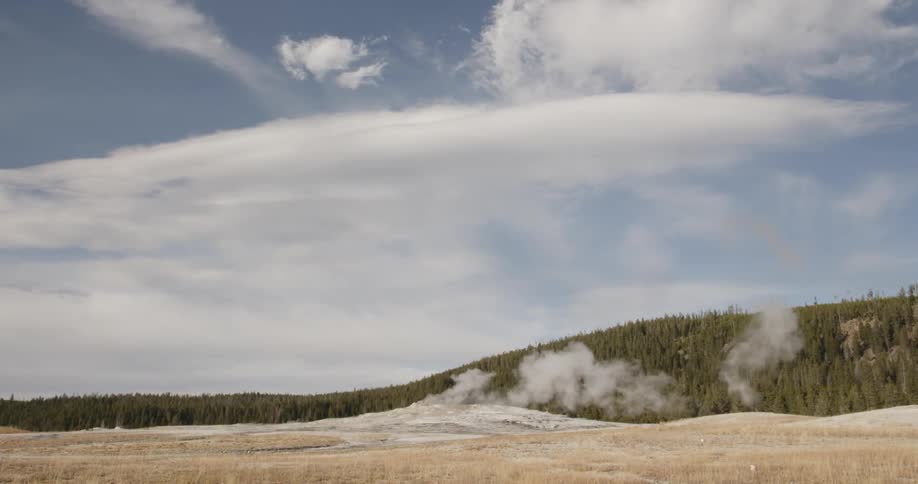 Steam rises from a geyser with clouds floating above