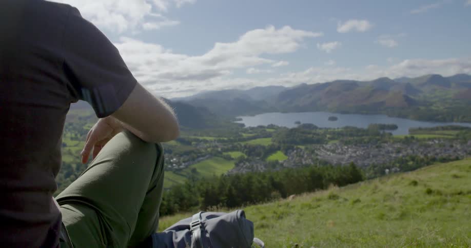 A man sits on the side of a hill looking down towards water