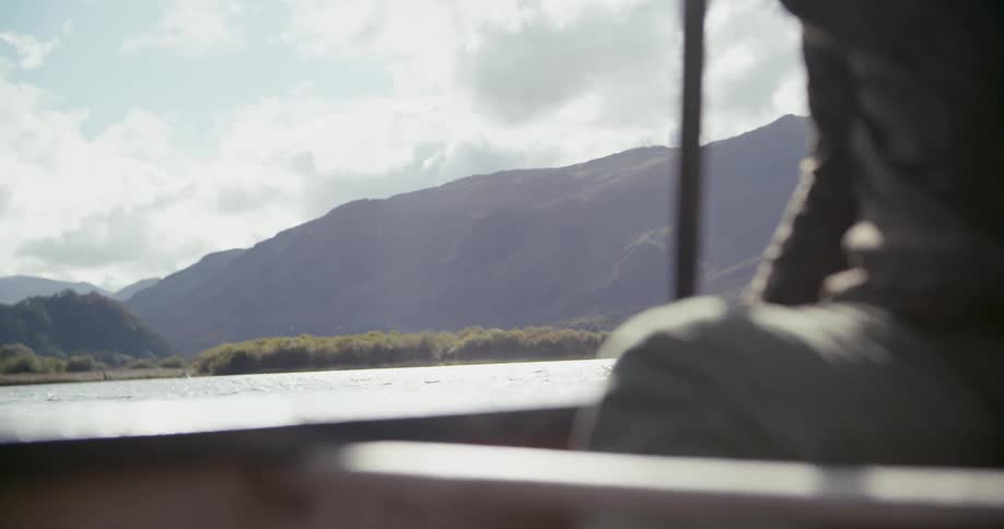 Man paddling in boat on lake surrounded by mountains on cloudy day