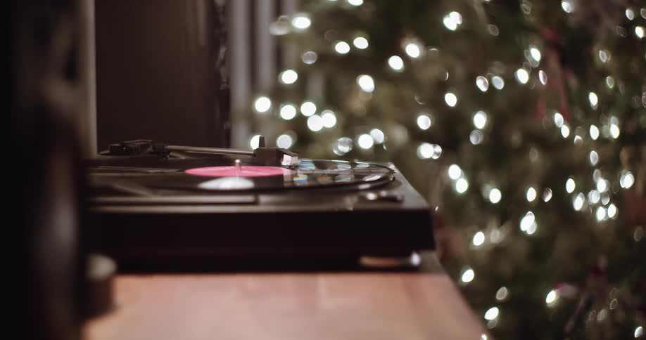 A record player spins in front of a christmas tree