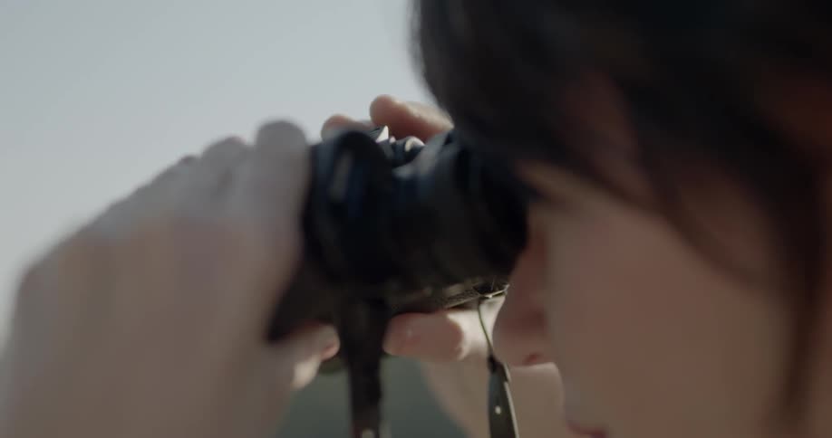 A woman using both hands is holding and adjusting binoculars to her eyes