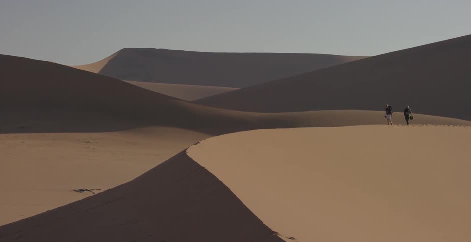 Two people cross a sandy desert