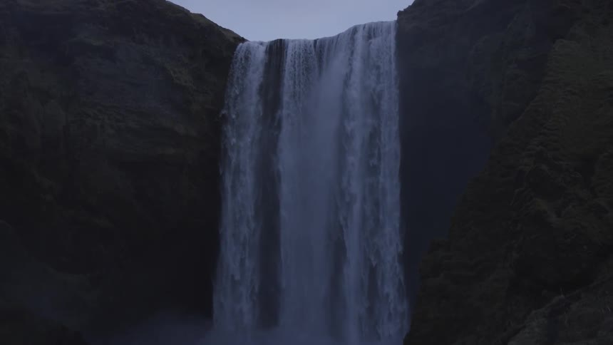 Top to bottom panning shot of waterfall flowing into a natural pool
