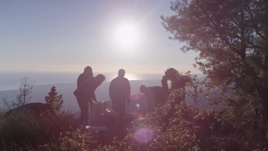 A group of friends set up a camp at the edge of the cliff at sunset