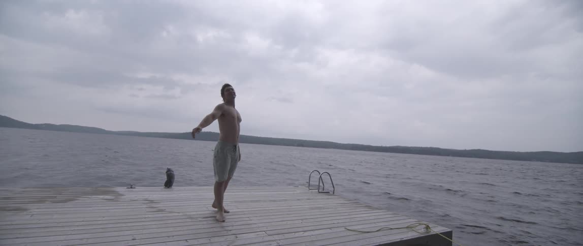 Shirtless man tossing football from waterfront deck