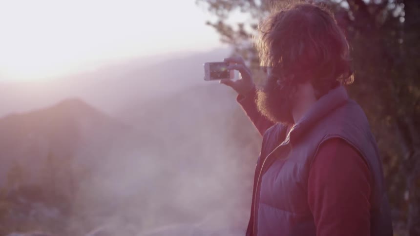 A bearded man trying to capture the morning sunrise with his phone