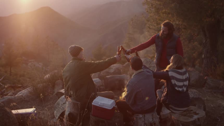 4 friends toast with beer bottles on the mountainside at dusk