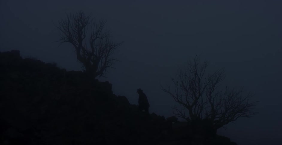 A silhouetted man walks up a hill at night