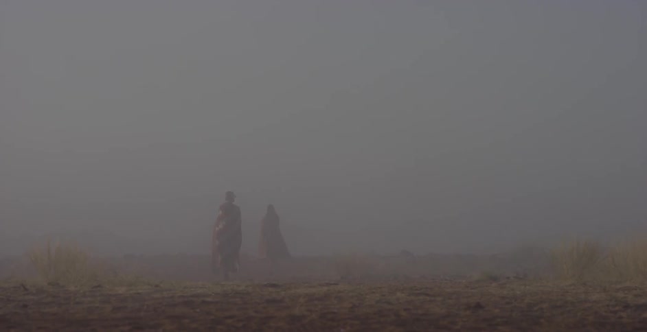 Two people in blankets or robes walk on sand on a hazy day