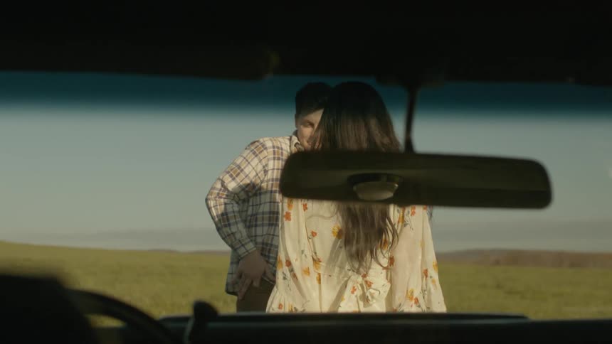 A man and woman sit on the hood of a car