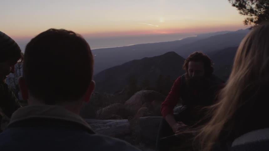 A couple of adults gathered around a campfire during sunset