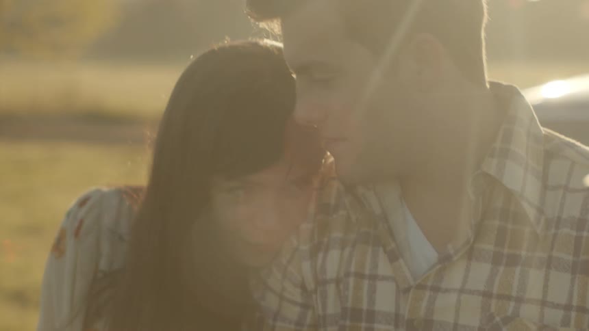 A woman puts her head on a man's shoulder while they sit outside