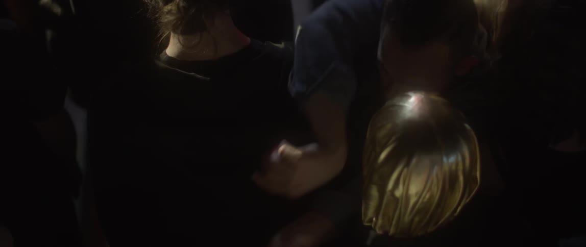 Man struggling to get through a crowd in a dark area with lights flashing around them