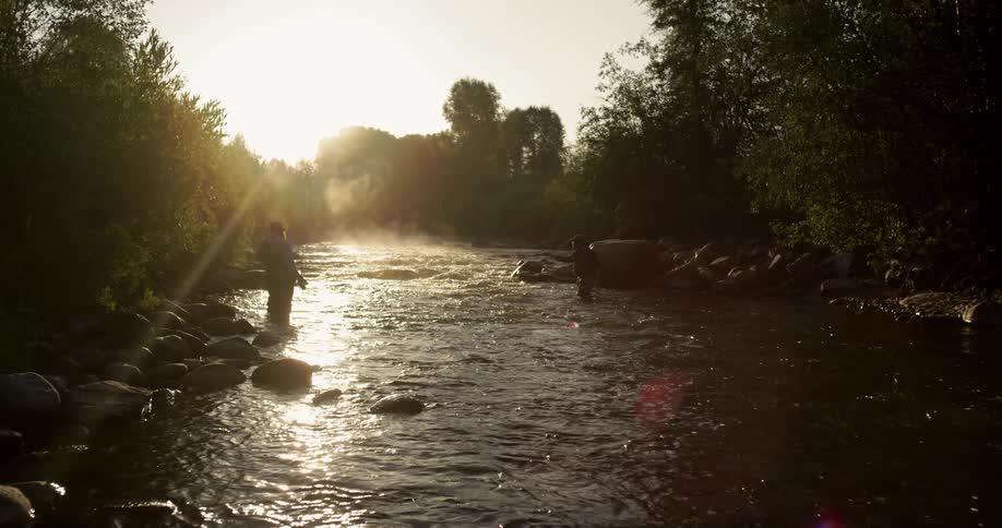 People stand in a river and fish at sunrise