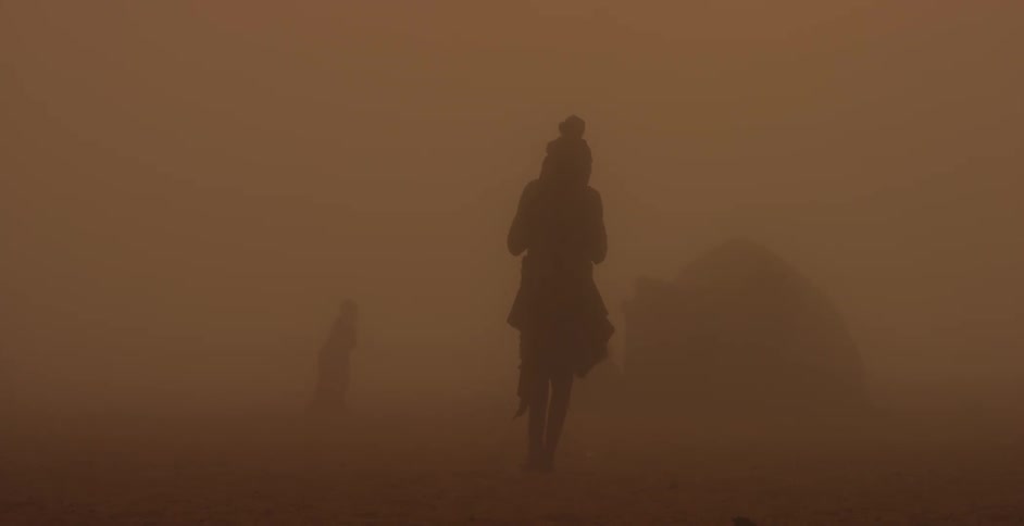 A silhouetted figure with a helmet walks across a hazy desert
