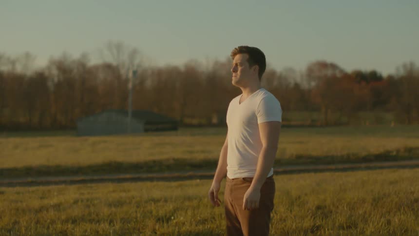 A man stands outside in a field looking sad