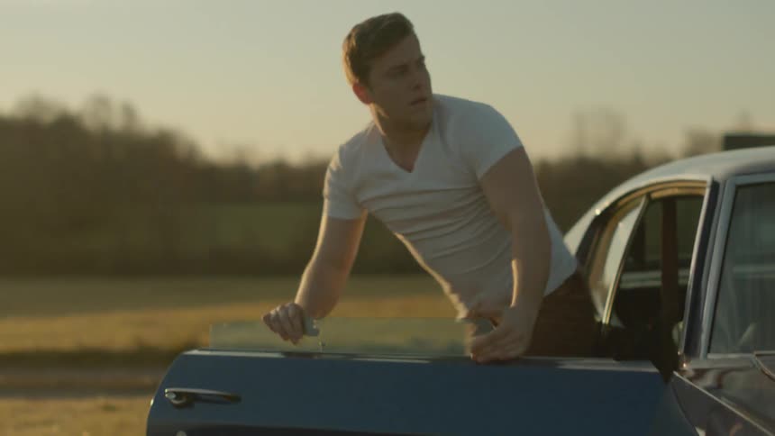 A man climbs out of the backseat of a sports car at sunset