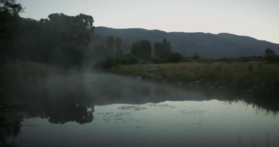 Mist drifts across a river at dusk