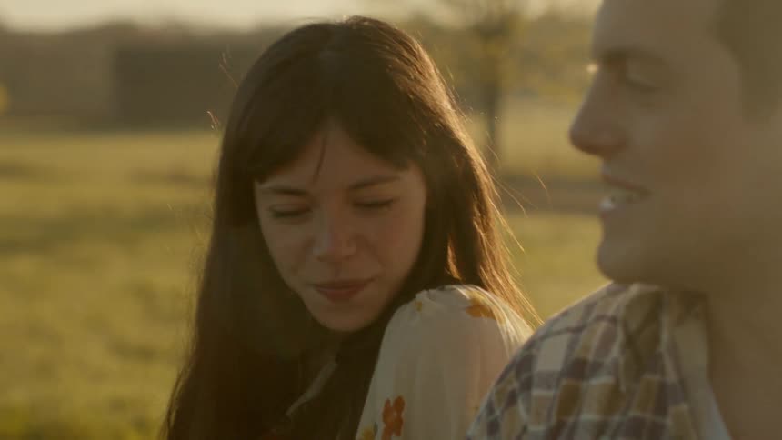 A man and woman talk in a rural field at sunset