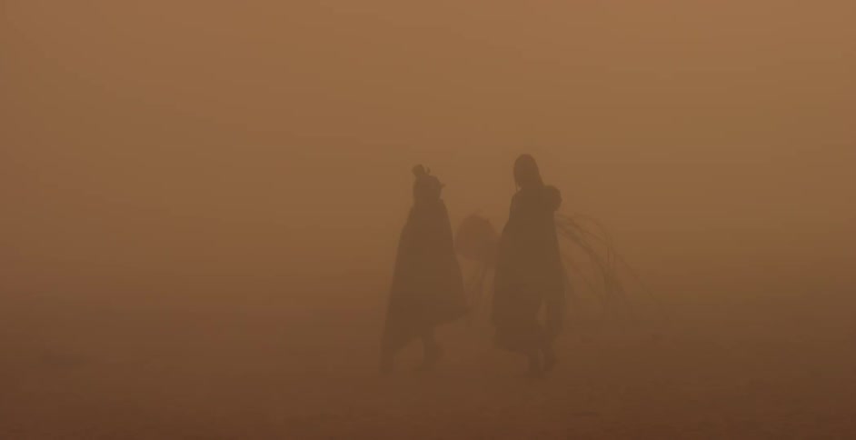 Two people walk in a desert on a dusty day