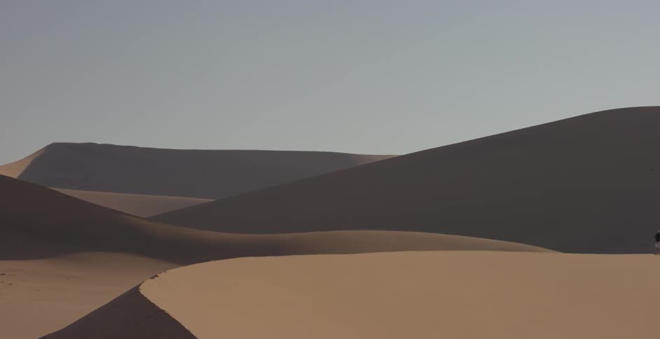 Two people are standing atop sand dunes in the desert