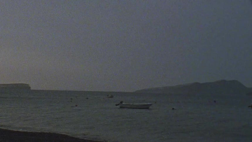 Couple walks onto beach with boats out in the water
