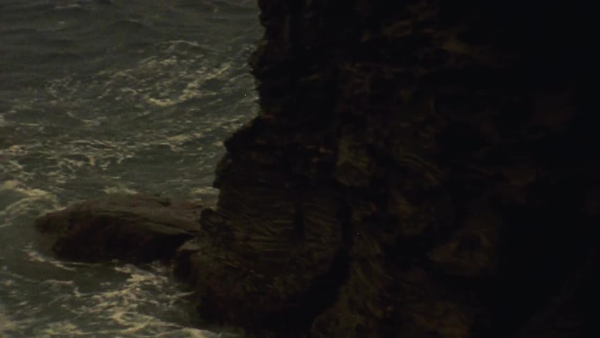 Ocean waves crashing up against rock cliffs on cloudy day